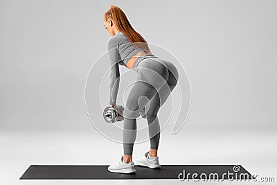 Athletic girl doing deadlift exercise for glutes on gray background. Fitness woman working out with dumbbells Stock Photo