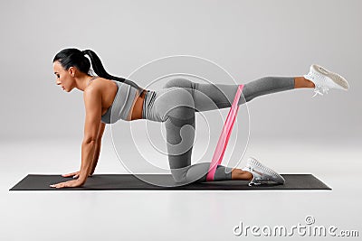 Athletic girl doing kickback exercise for glutes with resistance band. Fitness woman working out donkey kicks Stock Photo