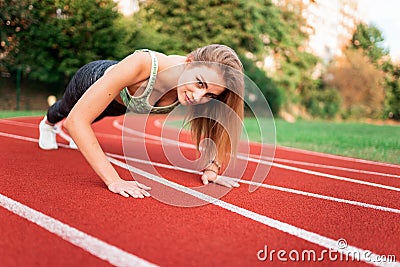 Athletic girl stands in the plank at the stadium runway. Stock Photo