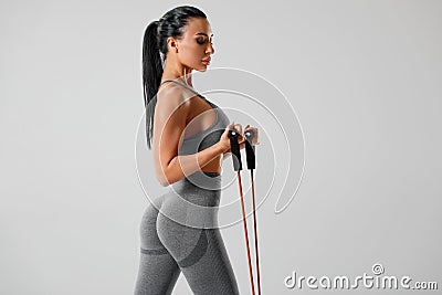Athletic girl working out with resistance band on gray background. Fitness woman exercises with expander Stock Photo