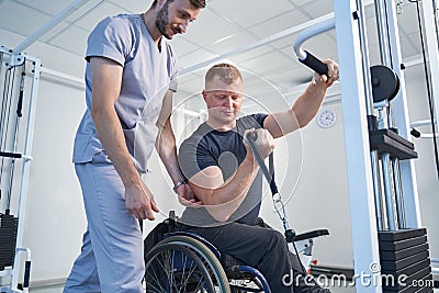 Athletic injured young man does weight exercise on cable simulator Stock Photo