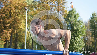 Athletic man doing push ups on parallel bars at sports ground in city park. Strong young muscular guy training outdoor Stock Photo