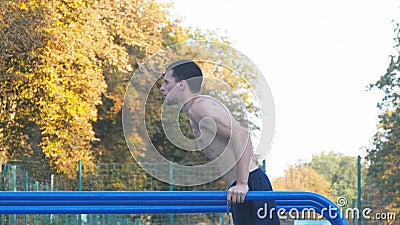 Athletic man doing push ups on parallel bars at sports ground in city park. Strong young muscular guy training outdoor Stock Photo