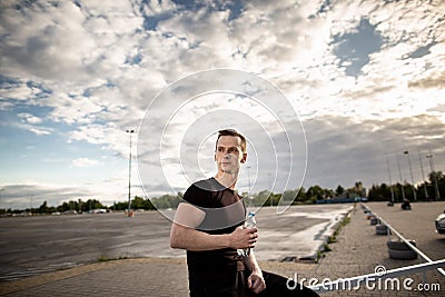 Athletic man sitting on the fence near the playground and holding a bottle of water. The man looks away Stock Photo