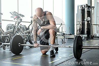 Portrait of a bald athletic man with a tattoo on his hand is preparing for the exercises with a barbell. Stock Photo