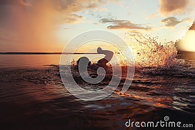 Athletic man is trained to swim in a lake at sunset. It flies a lot of water splashing Stock Photo