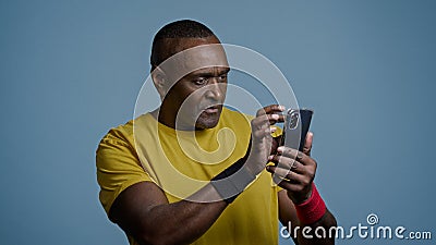 Athletic mature african american man in studio on blue background looking at mobile phone screen pensive male athlete Stock Photo