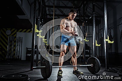 Athletic pumped man bodybuilder stands in front of bar in gym Stock Photo