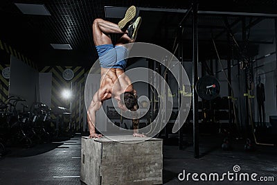 Athletic pumped man bodybuilder stands on his hands in gym Stock Photo
