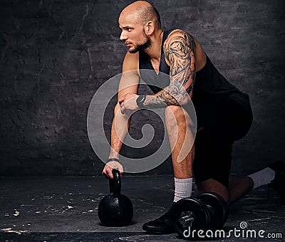 Sporty shaved head sporty male standing in knee and holds Kettlebell. Stock Photo