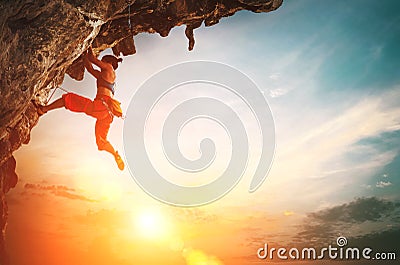 Athletic Woman climbing on overhanging cliff rock with sunset sky background Stock Photo