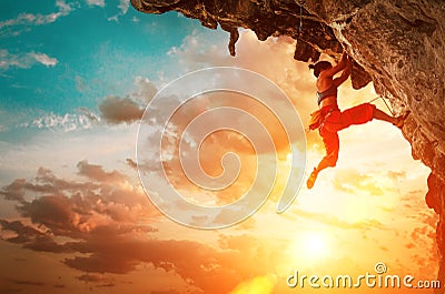 Athletic Woman climbing on overhanging cliff rock with sunset sky background Stock Photo