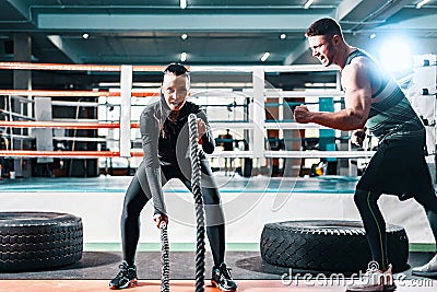 Athletic woman training on the ropes in the gym. male trainer mutates and helps to achieve success. concept to overcome Stock Photo