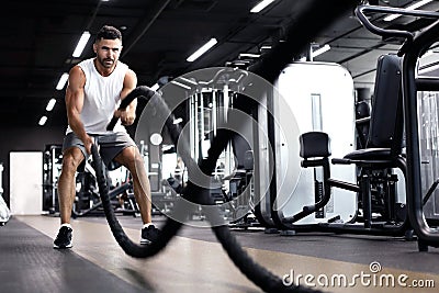 Athletic young man with battle rope doing exercise in functional training fitness gym Stock Photo