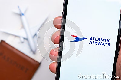 Atlantic Airways airline. A mobile phone and Atlantic Airways airline application in mans hand. There is a passport and Editorial Stock Photo