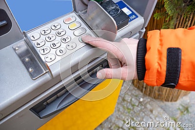 ATM user enters PIN while wearing orange jacket, hand presses button on ATM, importance secure transactions Secure banking Stock Photo