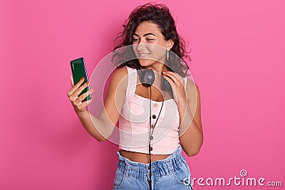 Attarctive woman having fun and making selfie picture using telephone, teen lady wearing black headphones around neck and rosy top Stock Photo