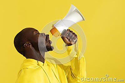 Attention! Black man shouting in megaphone on yellow background Stock Photo