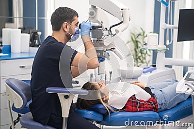 Attentive dentist looks at teeth of young woman through dental microscope Stock Photo