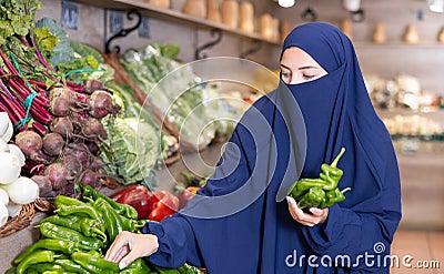 Attentive young Muslim woman purchaser choosing peppers in grocery store Stock Photo
