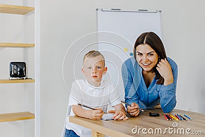 Attentive young woman tutor teacher helping little boy pupil with studying, correct mistakes explain learning material. Smiling Stock Photo