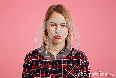 Attractive abused female model curves lips as being offended by close person, expresses her dissatisfaction, isolated over pink ba Stock Photo