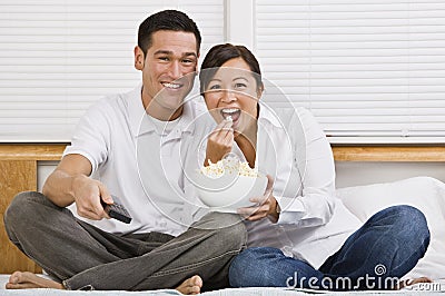Attractive Asian Couple Eating Popcorn in Bed Stock Photo