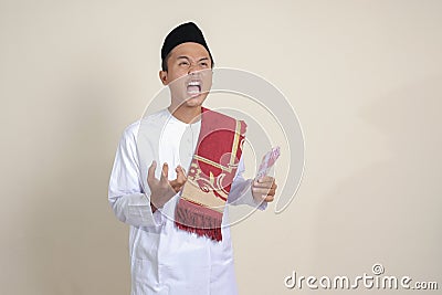 attractive Asian muslim man in white shirt making angry gesture showing one hundred thousand rupiah. Financial and Stock Photo