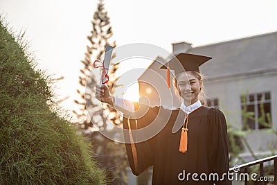 Attractive Asian Women Student Graduate in cap and gown celebrating with certificate in hand and so proud Stock Photo