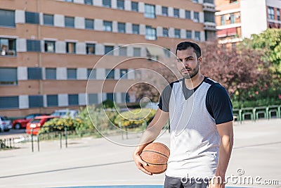 Attractive basketball player looks at camera smiling while posing with his ball on an urban court Stock Photo
