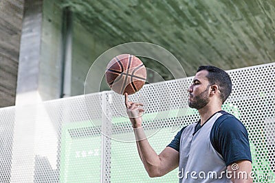 Attractive basketball player plays spinning his ball on a finger of his right hand while walking Stock Photo