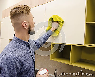 Attractive bearded man cleaning the handleless cabinet doors with a yellow rag in a modern kitchen Stock Photo