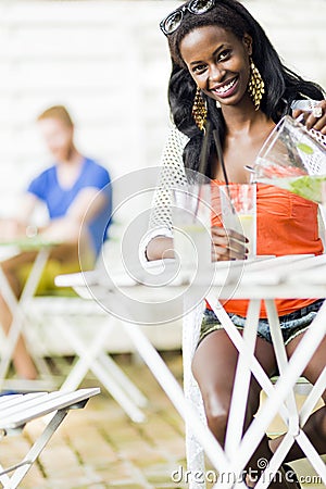 Attractive black woman sitting at a cafe table outdoors and drinking a refreshing beverage Stock Photo