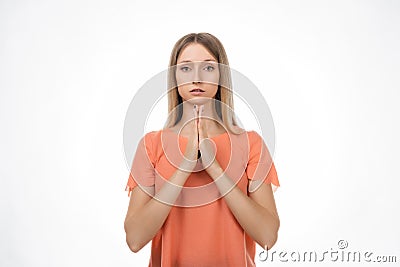 Attractive blond girl prays for wellness of family, keeps palms pressed together in praying gesture Stock Photo