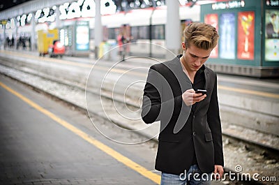 Attractive blond young man in station using cellphone Stock Photo