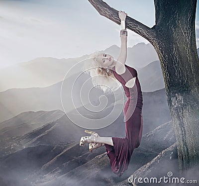 Attractive blonde lady hanging on a tree Stock Photo