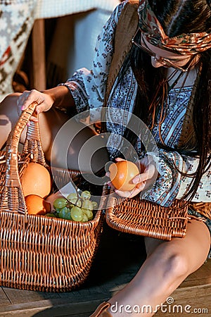 Attractive bohemian woman sitting on a floor with basket of fruits Stock Photo