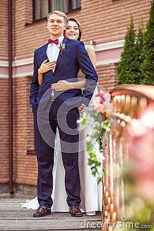 Attractive bride hugging handsome groom while standing on bridge Stock Photo