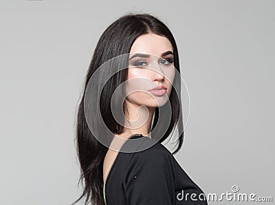 Attractive brunette in black dress on gray background. Beautiful young woman with smoky eyes and long black Stock Photo