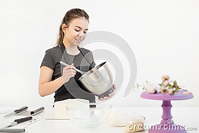 Attractive brunette girl pastry chef in apron whips cream cake in a metal bowl. Stock Photo