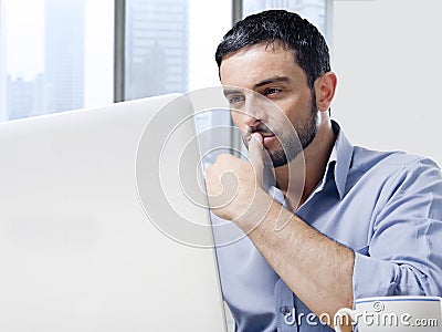 Attractive businessman working on computer at office desk in front of skyscraper window Stock Photo