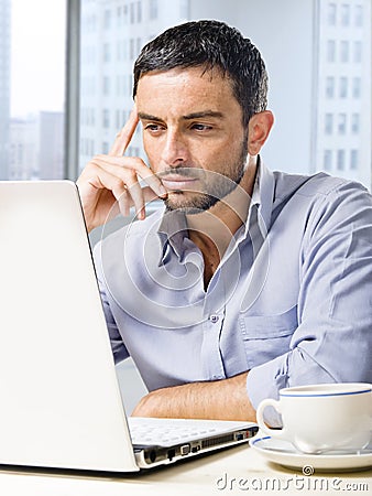 Attractive businessman working on computer at office desk in front of skyscraper window Stock Photo