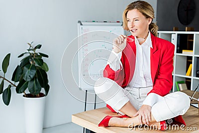 attractive businesswoman sitting on table and biting glasses Stock Photo