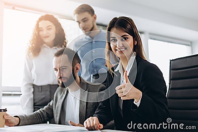 Attractive businesswoman smiling at the camera and showing thumb up during a business meeting Stock Photo