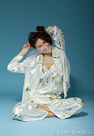 Attractive cheerful sleepy teen girl wearing pyjamas, isolated over blue background. Young pretty smiling woman in early before Stock Photo