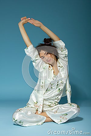 Attractive cheerful sleepy teen girl wearing pyjamas, isolated over blue background. Young pretty smiling woman in early before Stock Photo