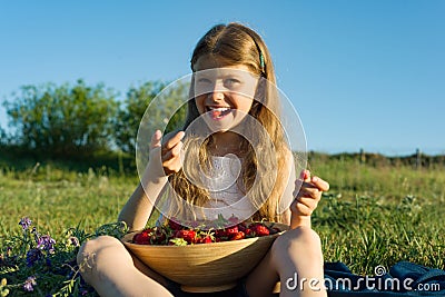 Attractive child girl eating strawberry. Nature background, green meadow, country style Stock Photo