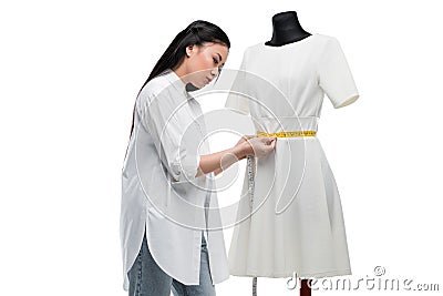 Attractive concentrated asian tailor measuring stylish white dress on dummy Stock Photo