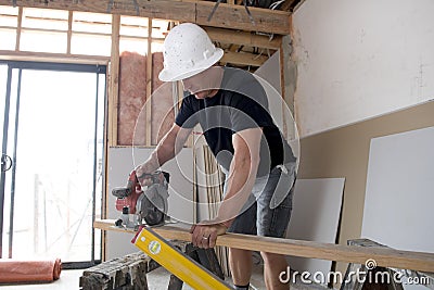 Attractive and confident constructor carpenter or builder man in protective helmet working happy cutting wood at industrial constr Stock Photo
