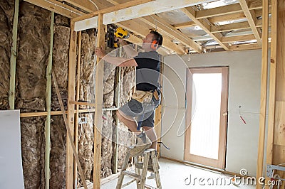 Attractive and confident constructor carpenter or builder man working wood with electric drill at industrial construction site Stock Photo